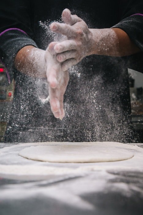 Un panadero agitando harina sobre masa