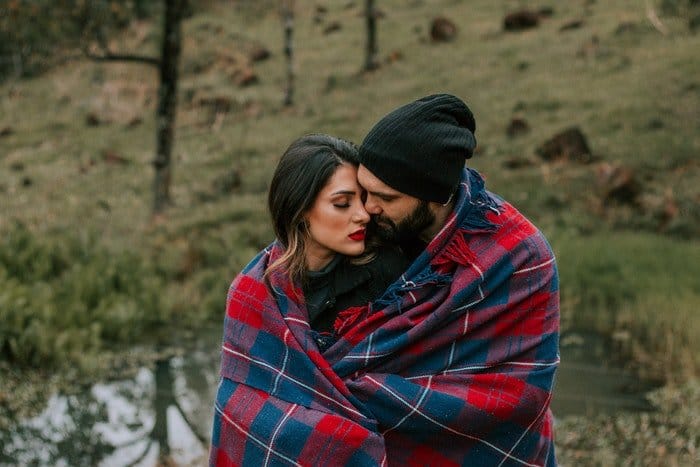 Una pareja abrazándose al aire libre, una manta a cuadros alrededor de ellos.