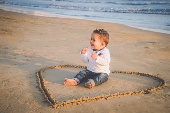 Un niño se sienta en medio de un corazón de amor dibujado en la arena, ideas creativas para fotografías de playa.
