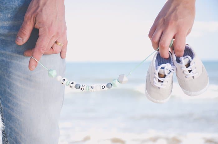 Cerca de una persona sosteniendo un collar y azadas de un bebé en una sesión de fotos en la playa 