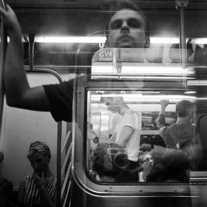 Reflexión del autorretrato tomada en el metro que superpone la reflexión y la imagen.  Fotografiado en monocromo en blanco y negro.