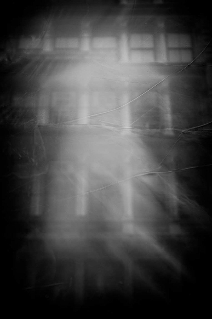 Una bruma fantasmal se proyecta sobre las ventanas de un edificio en fotografías de reflejos de calles en blanco y negro.