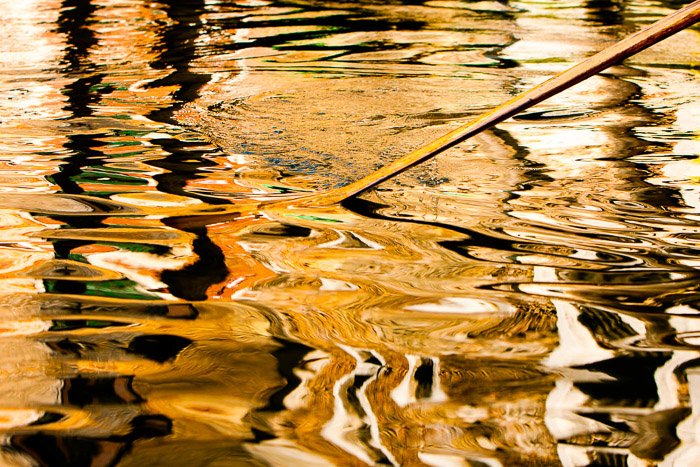 Un remo rompiendo la superficie de un río arrojando un reflejo entrecortado.  Fotografía callejera nocturna en color.
