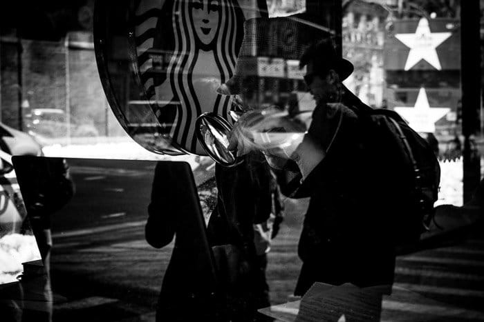 Fotografía en blanco y negro de un café Starbucks con un par superpuesto al cliente en el interior.  Reflexión del efecto de doble exposición.
