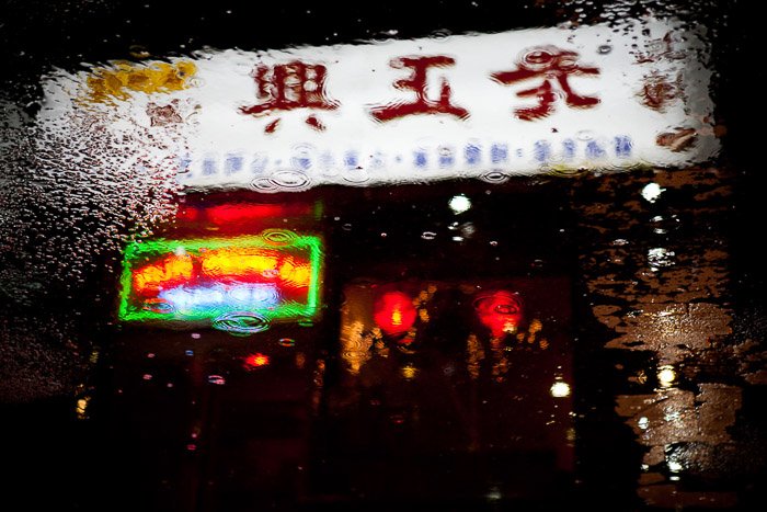 Comida para llevar chino con letreros de neón reflejados en los charcos de la calle.  Fotografía nocturna urbana