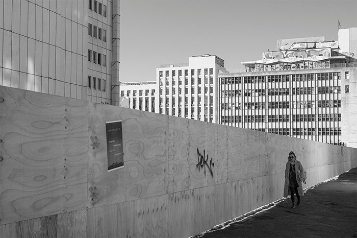Fotografía callejera en blanco y negro de un trabajador de la ciudad pasando por un sitio de construcción vacío .. Fotografía callejera creativa