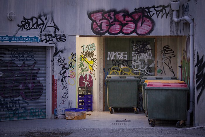 Fotografía callejera creativa de edificios con graffitis y cubos de basura.