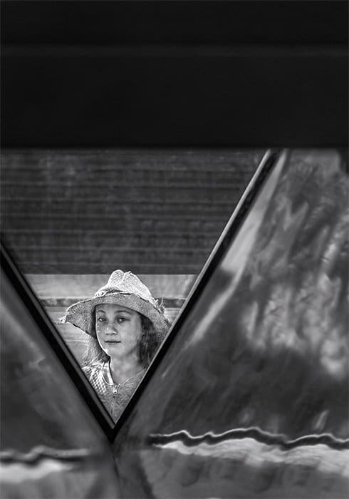 Fotografía en blanco y negro de una niña con sombrero blanco enmarcada por detalles arquitectónicos.  Fotografía callejera creativa