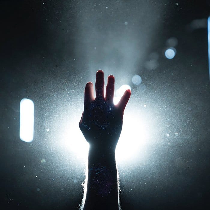 Foto de una mano que se extiende hacia arriba con una luz nítida en el fondo