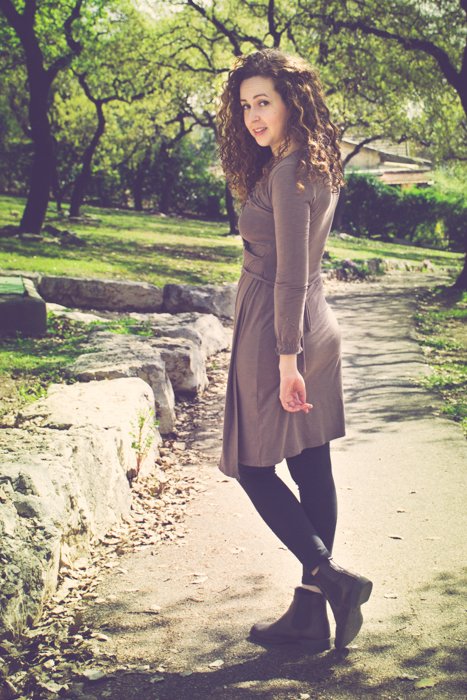 Morena de pelo rizado con un vestido marrón y botas mirando hacia atrás mientras camina por un camino de tierra en un parque - recortando fotos