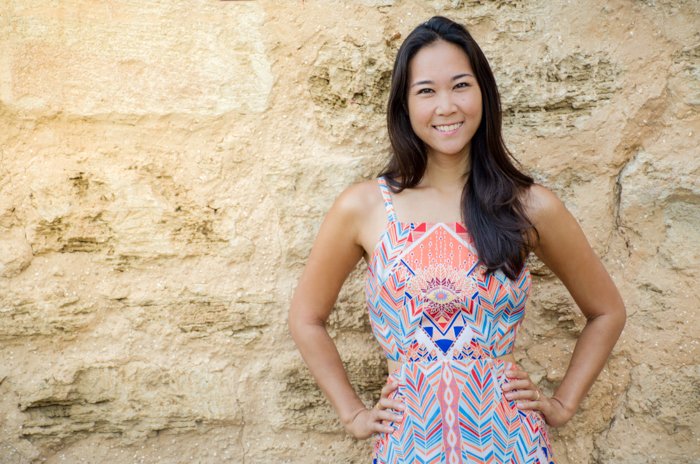 Sonriente mujer asiática en vestido estampado geométrico pastel de pie delante de un gran muro de piedra