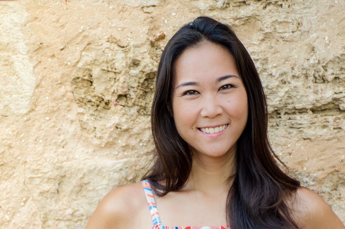 Foto recortada debajo de los hombros de la mujer asiática sonriente delante de un muro de piedra arenosa