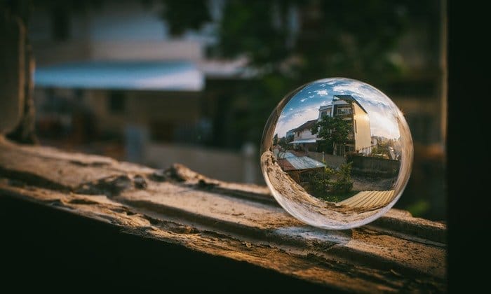 Un Lensball colocado en el marco de una ventana con una casa reflejada a través de él.