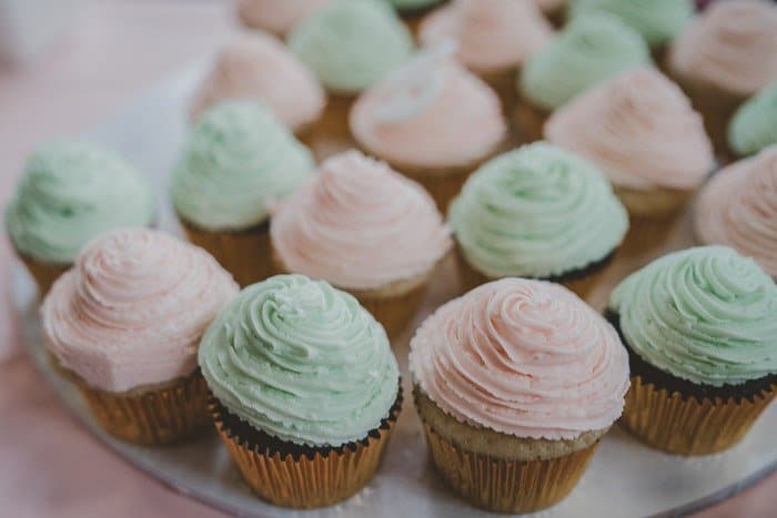 Foto brillante de un plato de cupcakes helados de color rosa y verde contra un fondo claro