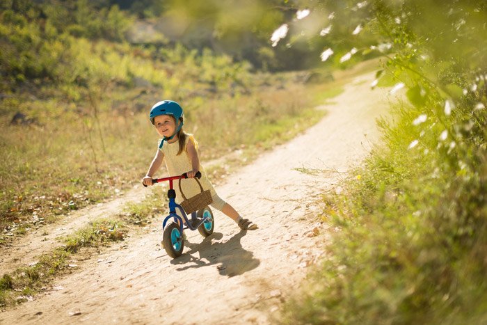 Foto de una niña con una bicicleta pequeña en un camino de tierra