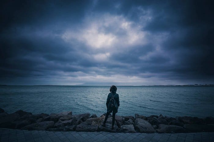 Una persona de pie frente a un lago con cielos oscuros.
