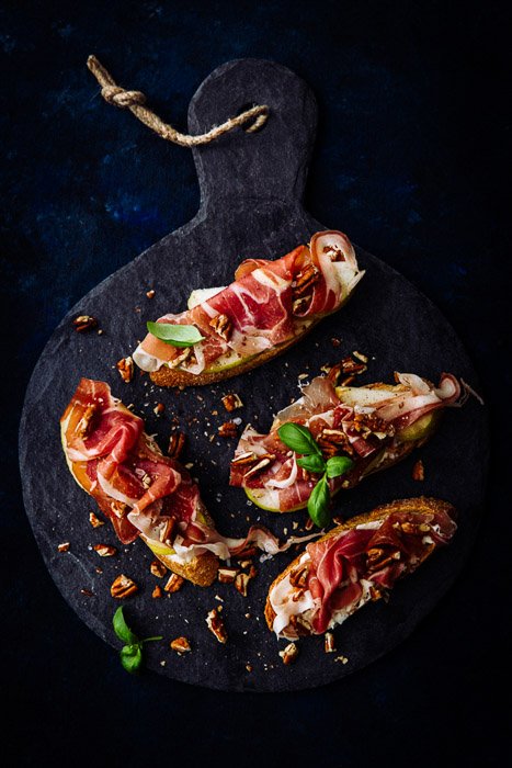Fotografía cenital de prosciutto crostini con nueces en un estilo de fotografía de comida oscura