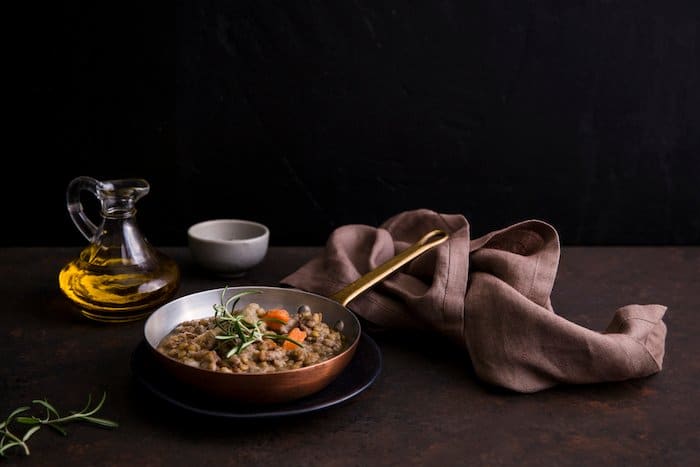 Una fotografía de alimentos oscuros configuración de naturaleza muerta de sopa de lentejas en una olla de cobre en la mesa