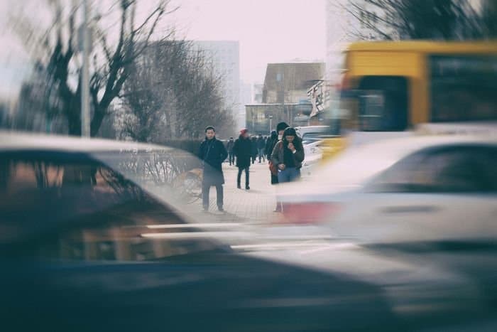 Foto de peatones en una acera con coches en movimiento en primer plano