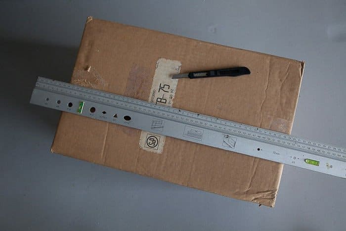 Fotografía cenital de una caja, una regla de acero y un cuchillo: herramientas que necesitas para hacer una caja de luz