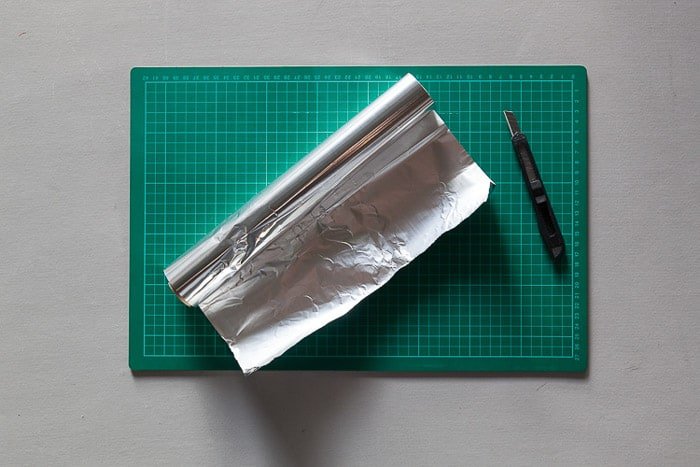 Una fotografía cenital de un tapete de corte, un rollo de papel de aluminio y un cuchillo Stanley: materiales para hacer una caja de luz para fotografía