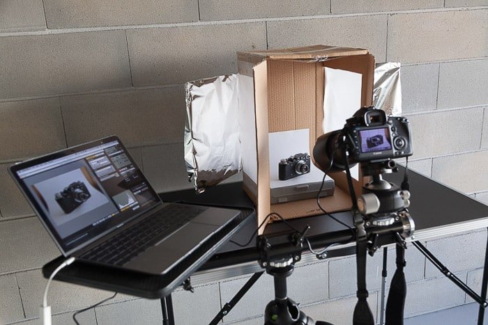 Una configuración de sesión de fotos que contiene una computadora portátil, una caja de luz de bricolaje, una cámara réflex digital en un trípode