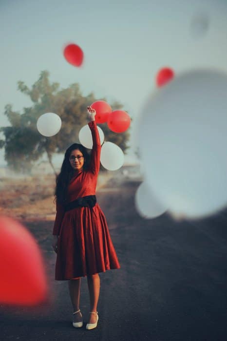 Un retrato de una niña con un vestido rojo de pie entre globos rojos y blancos flotantes - ideas para el fotomatón