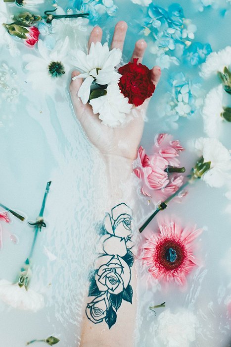 un brazo tatuado y flores en un baño de leche