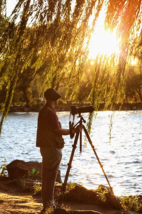 Un fotógrafo preparando una toma con una cámara y un trípode junto a un lago
