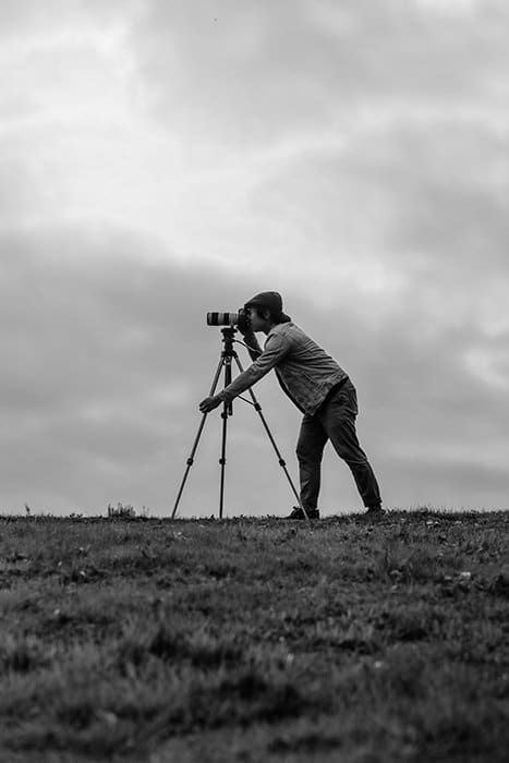 Un hombre tomando una foto a través de una DSLR en un trípode en un paisaje sombrío