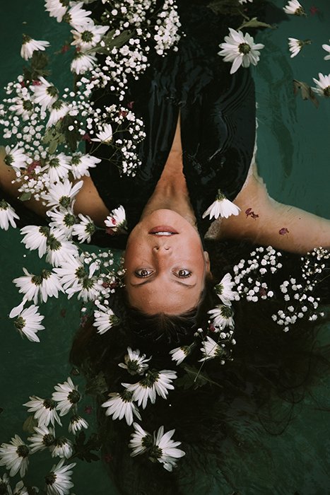 Foto de ensueño de una modelo femenina posando en el agua rodeada de flores blancas