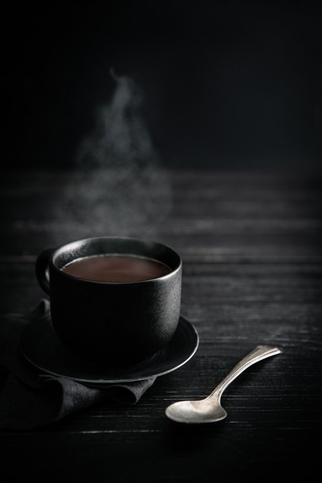 Foto de bebida elegante de una taza de café humeante contra un fondo oscuro