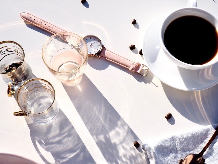 Fotografía cenital de una taza de café junto a tres vasos pequeños y un reloj