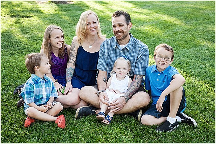 Una familia sonriente de seis, posando al aire libre sentada en el césped - fotografía emocional