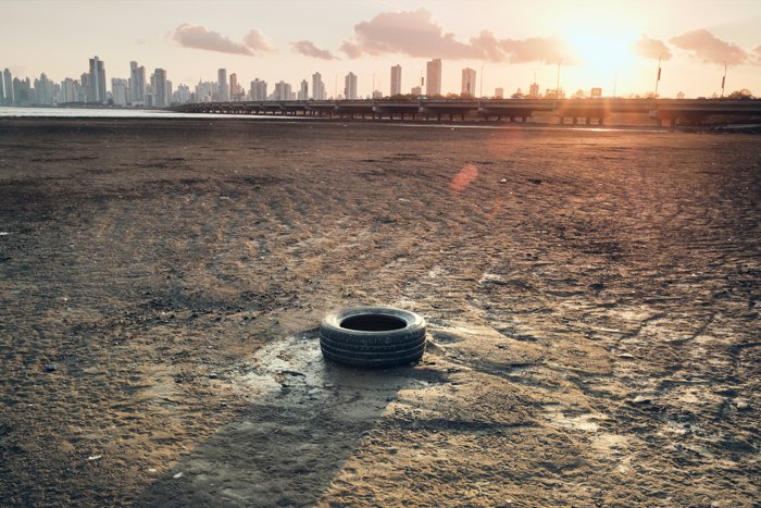 Una imagen documental de un neumático de goma en suelo reseco contra un horizonte urbano