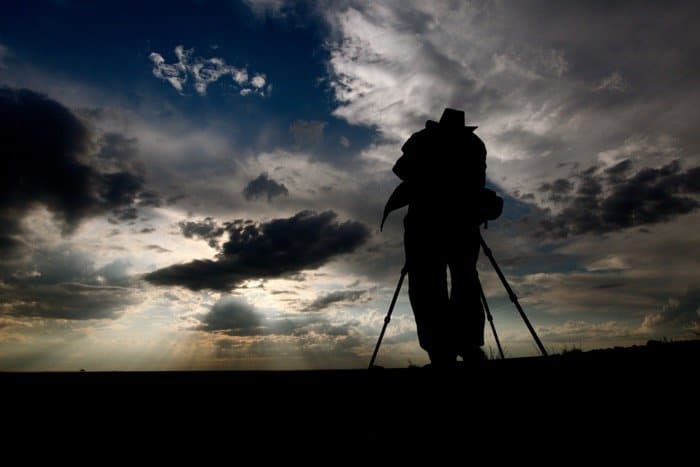 la silueta de un fotógrafo fotografiando un paisaje en un trípode