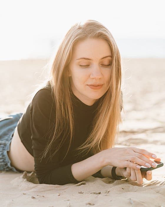 Joven mujer hermosa con el pelo largo se relaja en la playa de arena a contraluz.