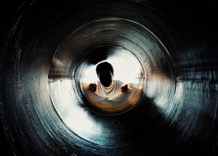 Un retrato sin rostro de un hombre mirando hacia arriba a través de un túnel oscuro