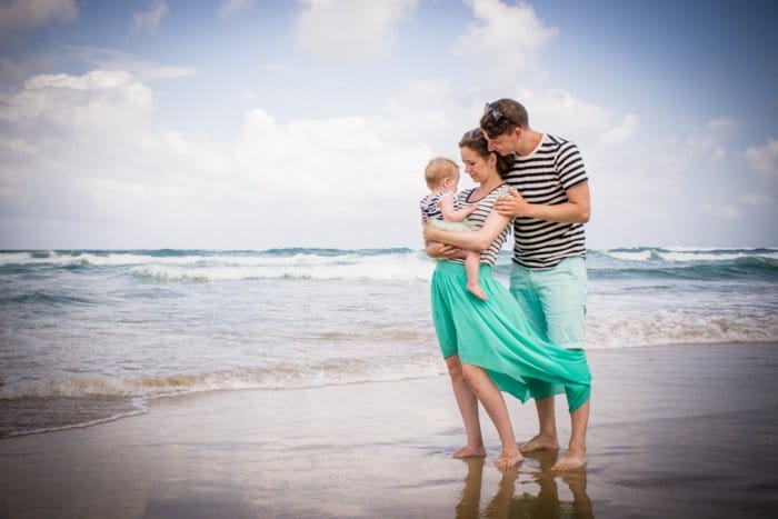 Foto de estilo de vida de una pareja con un bebé pequeño parado en la playa - composición para retratos familiares