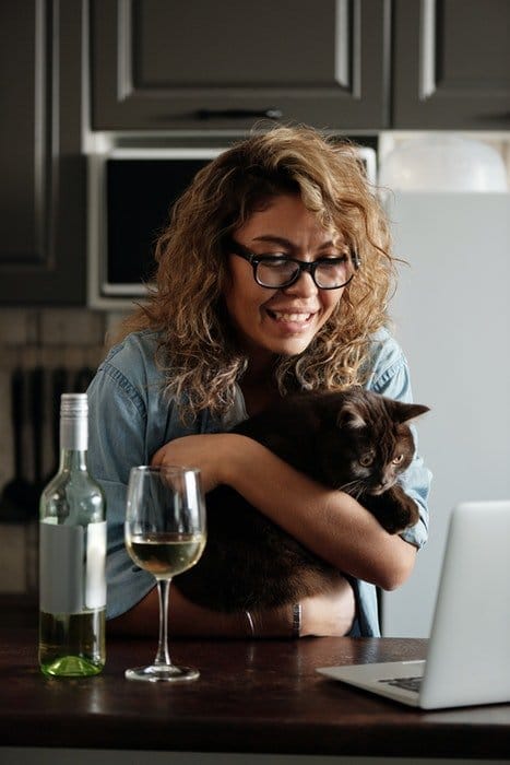 Lindo retrato de una chica de cabello rizado sosteniendo a su gato frente a su computadora portátil