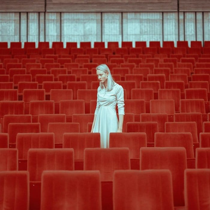 Una modelo femenina en blanco posando entre asientos de teatro rojos por v - estilo de fotografía de moda