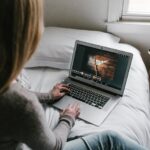 Una niña sentada en su cama y editando fotos en su computadora portátil