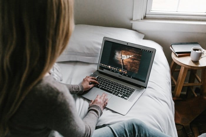 Una niña sentada en su cama y editando fotos en su computadora portátil