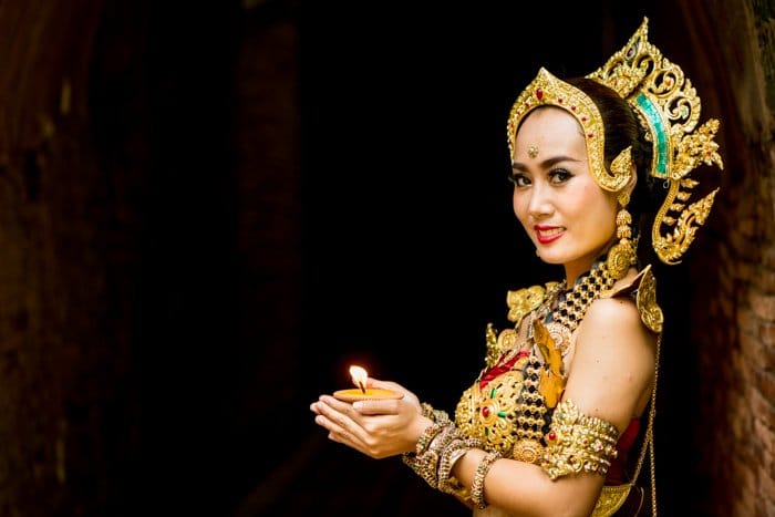 Una bailarina tailandesa sonriente bellamente disfrazada posa contra una figura oscura en el fondo del suelo