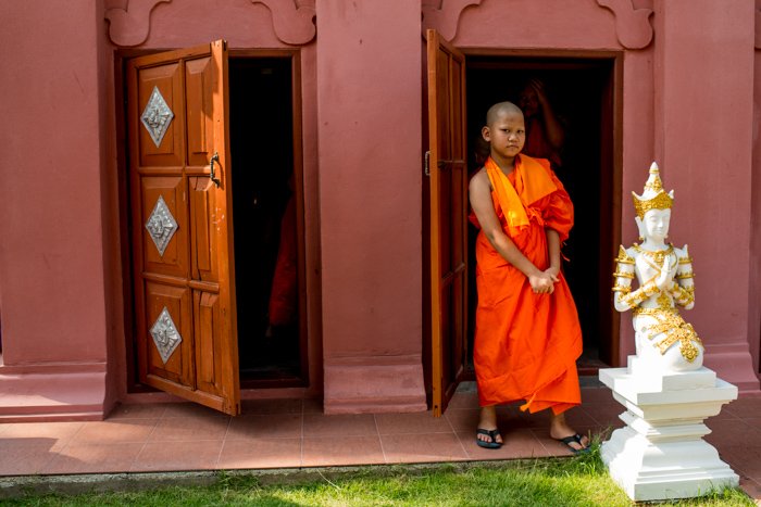 Un joven monje novicio con túnicas naranjas parado afuera de una puerta - composición de fotografía de figuras