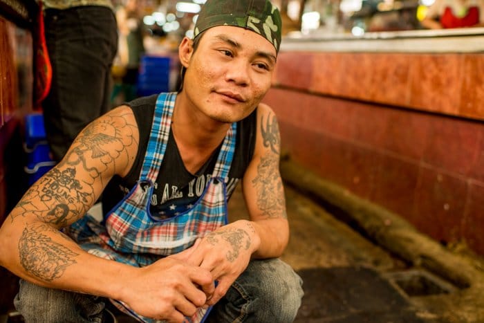 Un retrato callejero de un carnicero tailandés arrodillado en el suelo - composición fotográfica