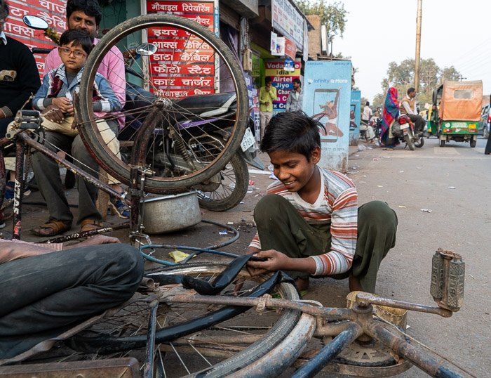 Un niño cambia un neumático de bicicleta en una calle de Agra, India.