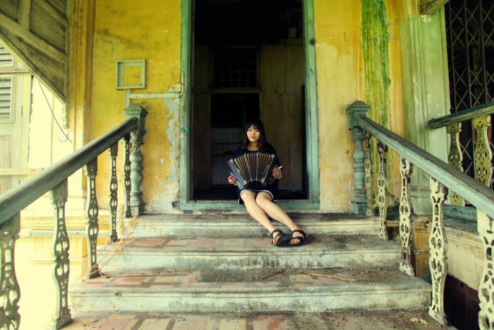 Foto de una niña tocando el acordeón en las escaleras de una casa abandonada