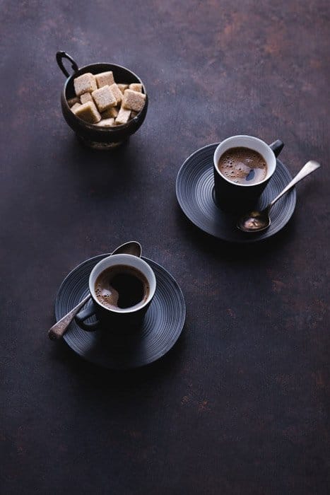 Un bodegón oscuro y atmosférico de fotografía gastronómica de bellas artes con dos tazas de café y azúcar