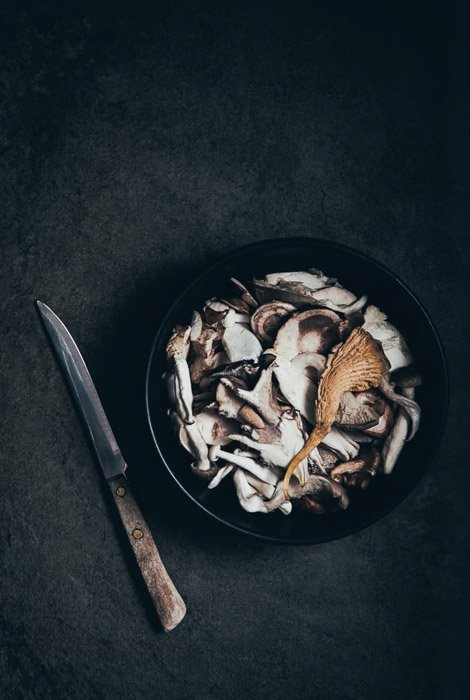 Una fotografía gastronómica oscura y atmosférica de bellas artes, bodegones de setas y un cuchillo